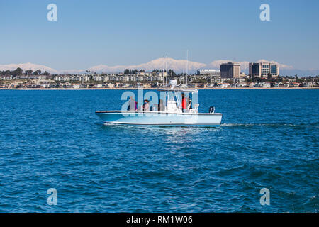 Small private whale watching boat off the coast of Newport Beach California with the Hoag Hospital & snowcapped San Gabriel Mountains in the background Stock Photo
