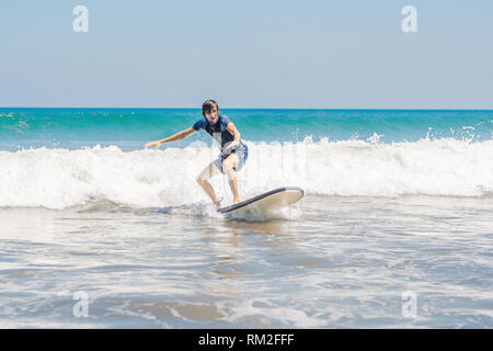 Young man, beginner Surfer learns to surf on a sea foam on the Bali island Stock Photo