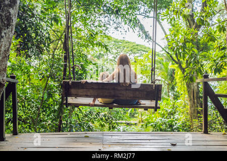 Mom and son on a swing in a tropical garden Stock Photo