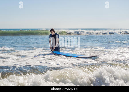Young man, beginner Surfer learns to surf on a sea foam on the Bali island Stock Photo