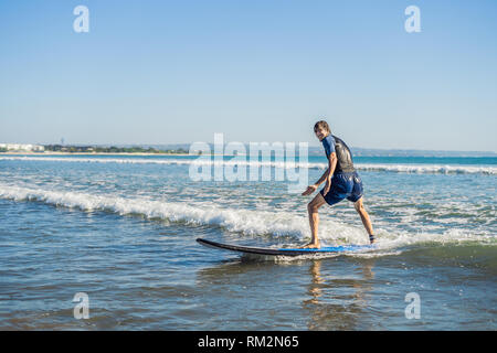 Young man, beginner Surfer learns to surf on a sea foam on the Bali island Stock Photo