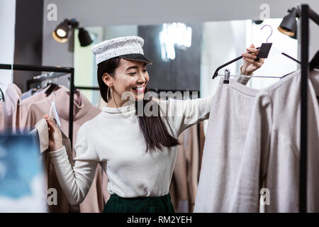 Brunette asian beautiful woman in a nice headwear choosing clothes Stock Photo