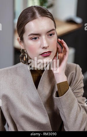 Beautiful long-haired pretty woman in a stylish jacket touching her earring Stock Photo