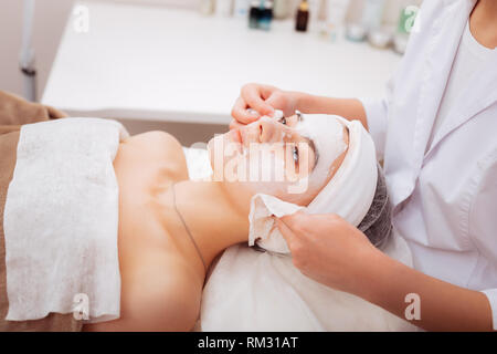 Professional nice cosmetologist removing a clay mask Stock Photo