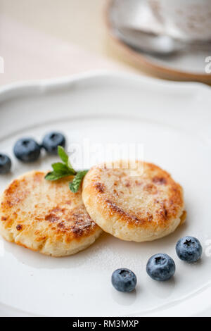 Cheesecake, fresh blueberry and cappuccino. Cottage cheese pancakes or curd fritters on white plate. Healthy and diet breakfast at sunrise Stock Photo