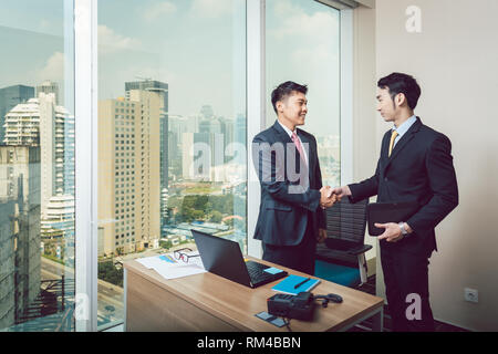 Two happy young businessmen shaking hands at workplace Stock Photo