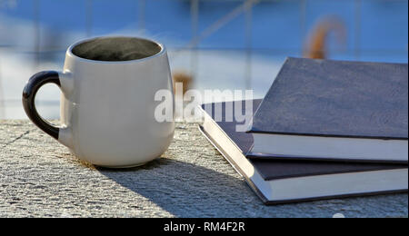 Winter background, a mug of hot drink and books in the shiny cold sno Stock Photo