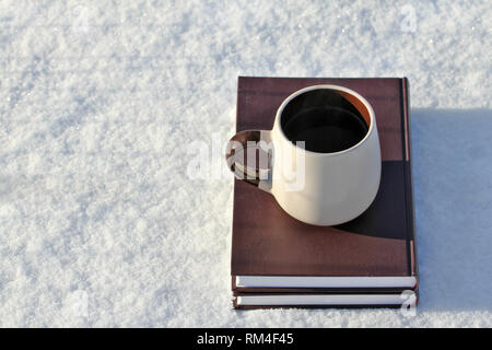 Winter background, a mug of hot drink and books in the shiny cold sno Stock Photo