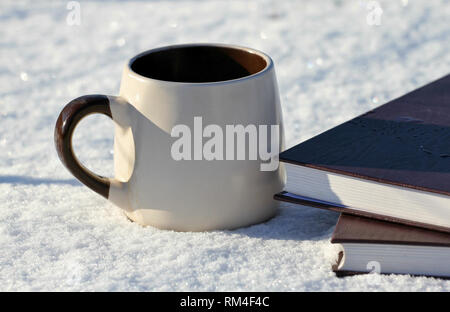 Winter background, a mug of hot drink and books in the shiny cold sno Stock Photo