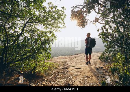 Young hiker overlooking view from rock. Landscape of Sri Lanka at sunset. Stock Photo