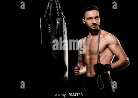 handsome boxer standing with jumping rope near punching bag isolated on black Stock Photo