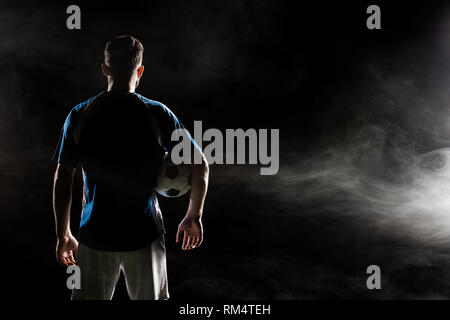 silhouette of man standing in uniform with ball on black with smoke Stock Photo