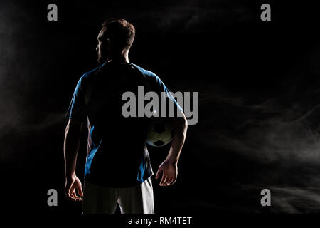 silhouette of football player standing with ball on black with smoke Stock Photo