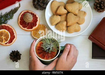 Warm composition on the table, a red scarf, dried oranges, heart-shaped cookies, a cup of hot tea with a slice of grapefruit and pine branches Stock Photo