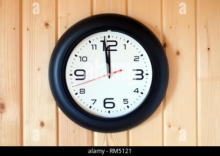 Big round wall clock with a black rim with arrows showing twelve o'clock hangs on brown wooden wall from vertical planks horizontal view indoor close- Stock Photo