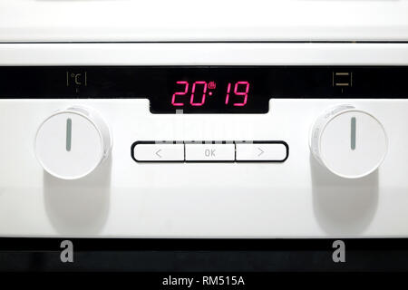 Control panel with red digits on electronic timer display, buttons and round knobs on modern white kitchen electric stove front view closeup Stock Photo