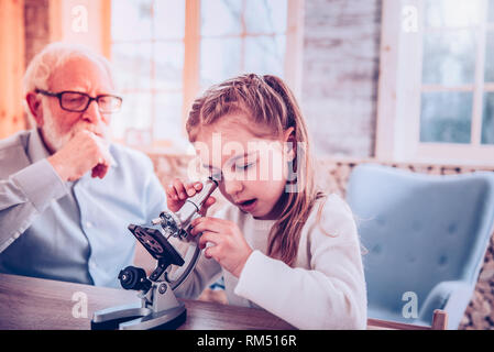 Smart schooler with nice hairstyle using microscope Stock Photo