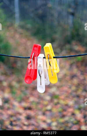 Three colored clothespins hanging on black rope on a blurred background in autumn day outdoors vertical view closeup Stock Photo