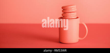 sweet macarons in cup on trendy Living coral background. Pantone color of the year 2019 concept Stock Photo