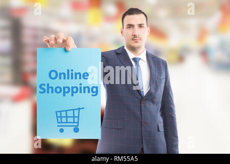 Salesman wearing suit and tie holding online shopping blue paper in hand with cart drawing as digital commerce concept Stock Photo