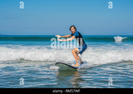 Young man, beginner Surfer learns to surf on a sea foam on the Bali island Stock Photo