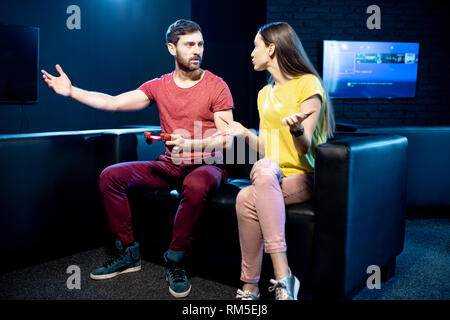 Woman offended by a boyfriend playing video games with gaming console sitting on the couch in the dark playing room Stock Photo