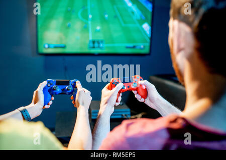 Young couple playing football game with gaming console sitting on the couch at the playing club, back view with tv screen Stock Photo