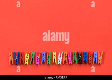 A row of colorful wooden clothespins on a red background and copy space. Stock Photo