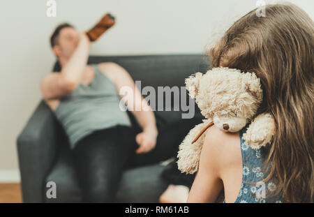 Little girl with toy standing in front of her drunk father. Stock Photo