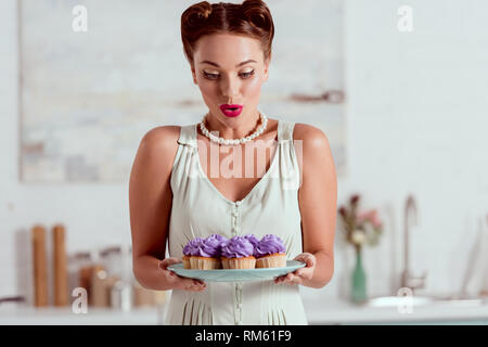 Beautiful pin up girl looking at plate full of cupcakes Stock Photo