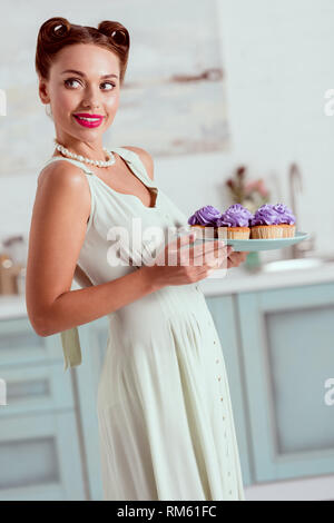 Beautiful pin up girl holding plate full of cupcakes Stock Photo