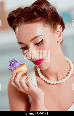 Beautiful pin up woman in pearl necklace holding homemade cupcake Stock Photo