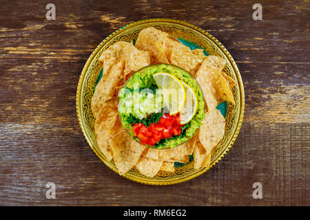 Fresh green guacamole with lime juice and nachos and on wood background Stock Photo