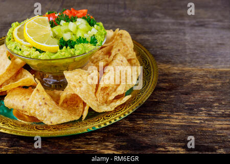Guacamole with tortilla chips in fresh ingredients over vintage rusty a bowl on a dark wood background. Top view with copy space. Stock Photo