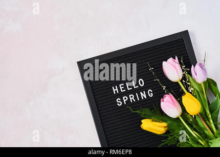Spring concept. Pink and yellow tulips on letterboard with quote Hello Spring over pink background. Top view with copy space for text. Flat lay. Stock Photo