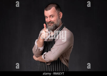 Mature bearded man in apron pointing with finger at camera Stock Photo