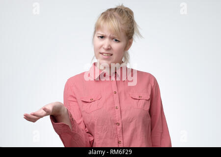 Woman with blonde hair looking in confusion, shrugs shoulders as do not know answer, being clueless Stock Photo