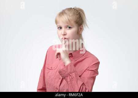 ovely blonde female asks to keep secret information confidential, dressed in pink shirt Stock Photo