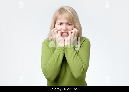 Woman wearing green sweater scared, afraid and anxious biting her finger nails, looking at camera Stock Photo
