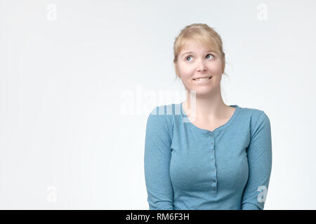 Young beautiful playful blonde woman with cunning tricky glance smiling looking up Stock Photo
