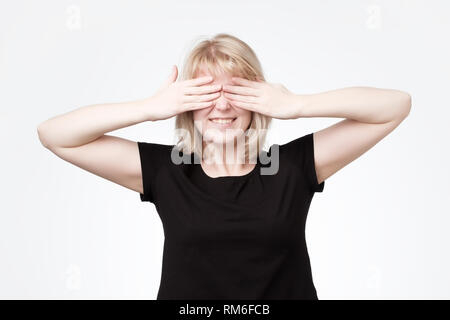 Woman covering eyes with hands and smiling broadly, being intrigued while waiting for surprise Stock Photo