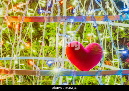 A little red heart shape pillow on decorate colorful light bulbs in garden. Stock Photo