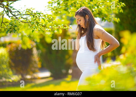 Pregnant woman in beautiful garden looking down at her belly Stock Photo