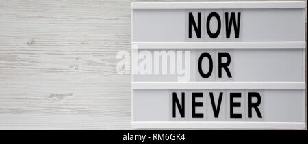Lightbox with text 'Now or never' word on modern board on a white wooden background, top view. Copy space. Stock Photo