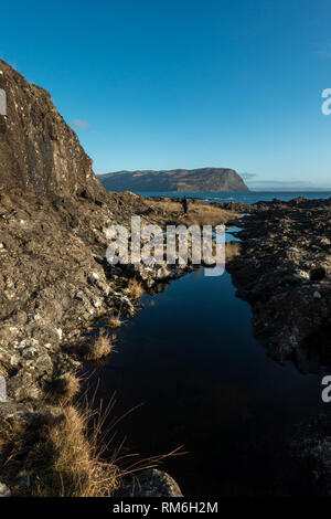 Person walking the coastal path from Carsaig to Lochbuie past stunning rock pools reflecting the blue sky, Isle of Mull coastline, Scotland Stock Photo