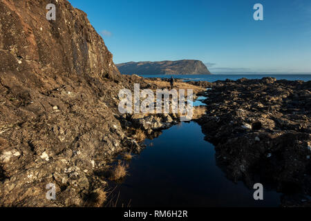Person walking the coastal path from Carsaig to Lochbuie past stunning rock pools reflecting the blue sky, Isle of Mull coastline, Scotland Stock Photo