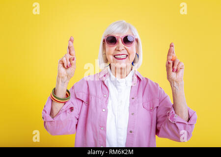 Stylish modern retired woman with bright manicure having fingers crossed Stock Photo