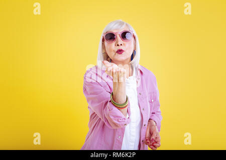 Lovely elderly lady wearing bright pink jacket sending air kiss Stock Photo