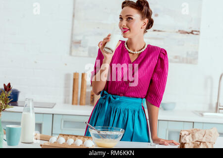 Elegant pin up girl drinking milk standing near kitchen table with different products Stock Photo