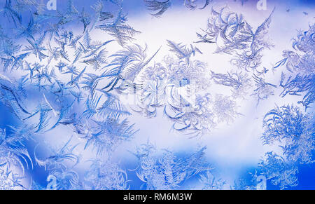 beautiful frosty pattern with various ornate patterns on the transparent glass on the winter window in delicate lilac and blue tones Stock Photo